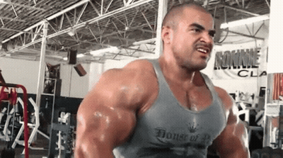 A Very Muscular Man Is Lifting Weights In A Gym Wearing A Tank Top That Says House Of Bodybuilding . GIF
