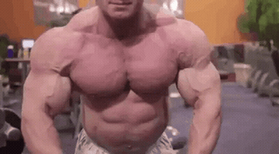 A Very Muscular Man Is Standing In A Gym With His Arms Outstretched . GIF