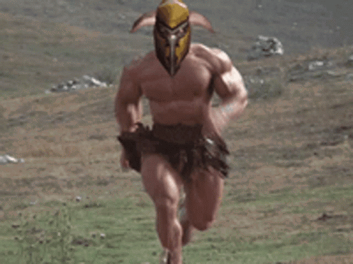 A Very Muscular Man With A Helmet On His Head Is Running Through A Grassy Field . GIF