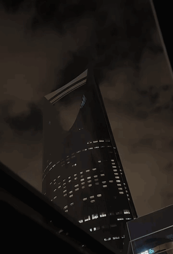 A Very Tall Building Is Lit Up At Night With A Dark Sky GIF