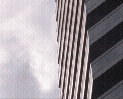 A Very Tall Building With A Cloudy Sky Behind It GIF