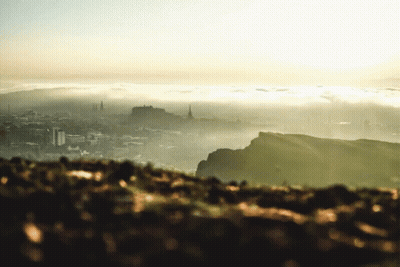 A View Of A City From A Hill With The Sun Shining Through The Clouds GIF