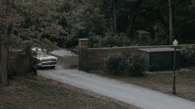 A Vintage Car Is Driving Down A Road With A Brick Wall In The Background GIF