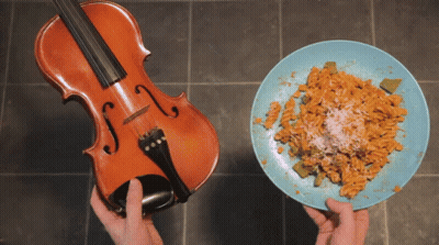 A Violin Next To A Plate Of Pasta With Cheese GIF