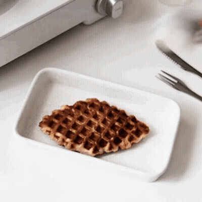 A Waffle On A White Plate Next To A Fork And Knife . GIF