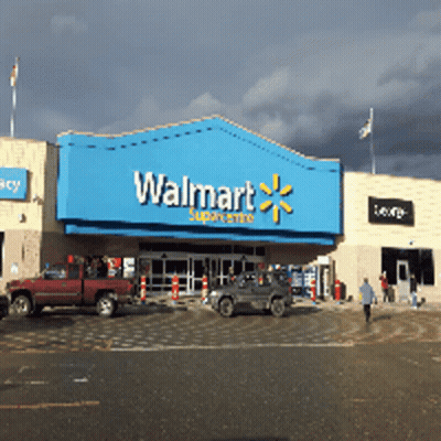A Walmart Store With Cars Parked In Front Of It On A Cloudy Day GIF
