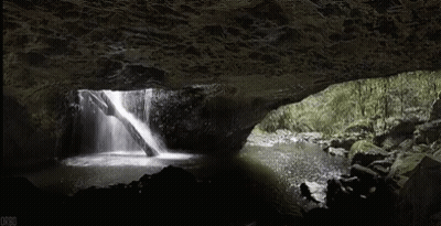 A Waterfall Is Coming Out Of A Cave In The Woods GIF