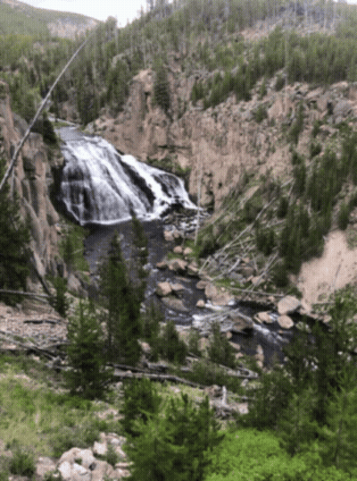 A Waterfall Surrounded By Trees And Rocks In A Valley GIF