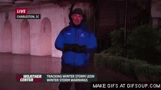A Weatherman In A Blue Jacket Is Standing In Front Of A Building In The Dark . GIF
