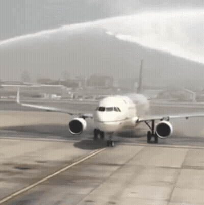 A White Airplane Is Being Sprayed With Water On The Tarmac GIF