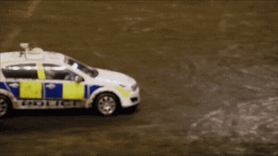 A White And Blue Police Car Is Driving Down A Road GIF