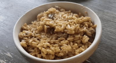 A White Bowl Filled With Rice And Meat Is On A Wooden Table GIF