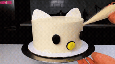 A White Cake With Black Circles And Ears Is Being Decorated By A Person GIF