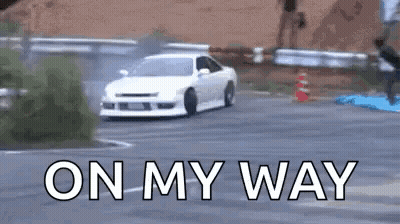 A White Car Is Drifting Down A Road With The Words `` On My Way '' Written On The Bottom . GIF