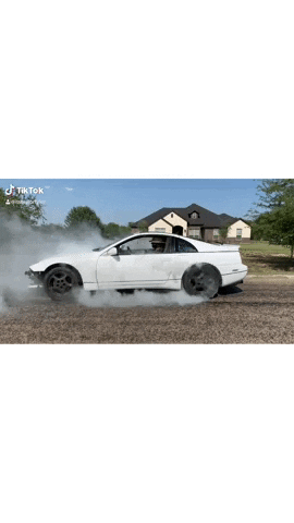 A White Car Is Drifting On A Gravel Road With Smoke Coming Out Of It . GIF