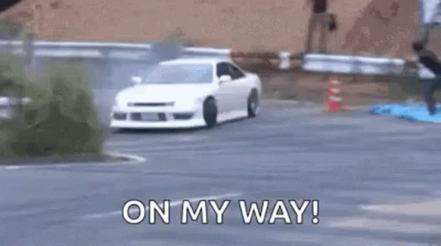 A White Car Is Drifting On A Road With People Standing On The Side Of The Road . GIF