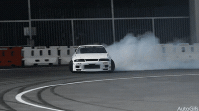 A White Car Is Drifting On A Track And Smoke Is Coming Out Of The Tire GIF