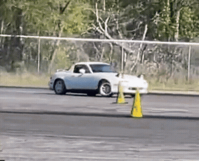 A White Car Is Drifting On A Track Next To Yellow Cones . GIF