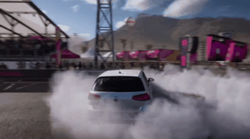 A White Car Is Drifting On A Track With Smoke Coming Out Of The Tires GIF