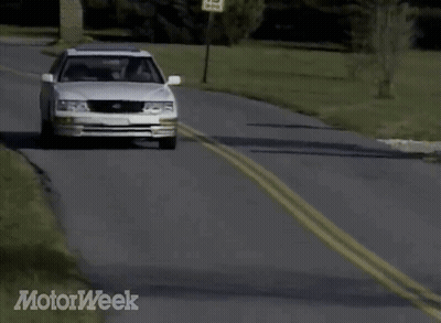 A White Car Is Driving Down A Road With Motorweek Written In The Corner GIF