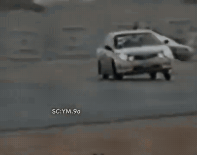 A White Car Is Driving Down A Road With The Words Sc Ym 90 On The Bottom Right Corner . GIF