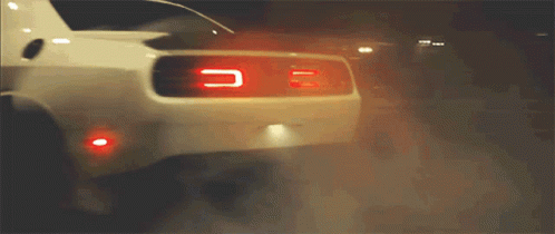 A White Car Is Driving Down A Street At Night GIF