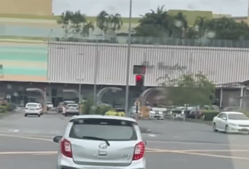 A White Car Is Driving Down A Street With A Red Light In The Background GIF