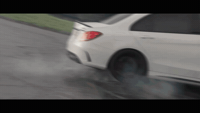 A White Car Is Driving Down A Wet Road With Smoke Coming Out Of The Tire GIF