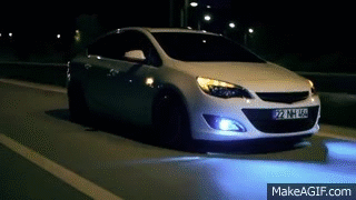 A White Car Is Driving On A Highway At Night . GIF