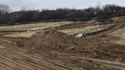A White Car Is Driving Through A Dirt Field With A Fence In The Background GIF