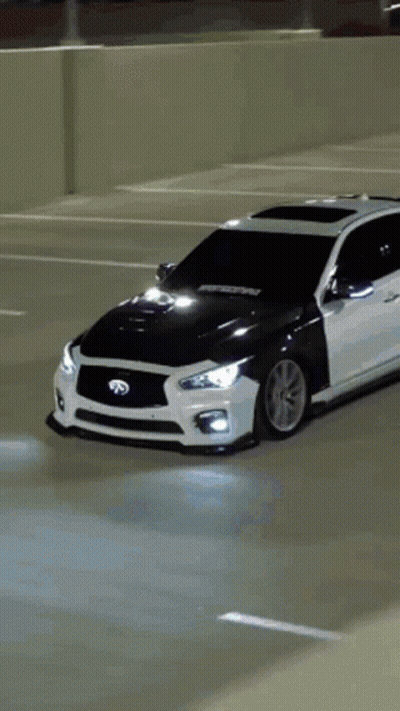 A White Car Is Parked In A Parking Lot With A Black Hood GIF