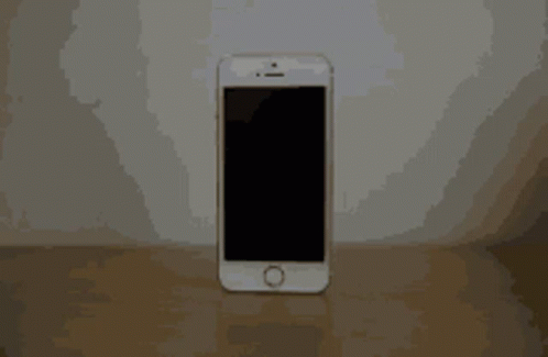 A White Cell Phone With A Black Screen Is Sitting On A Wooden Table GIF