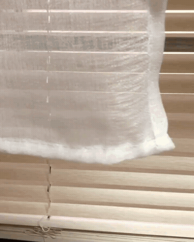 A White Curtain Is Hanging On A Window With Blinds GIF