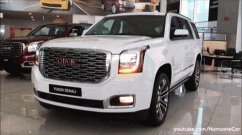 A White Gmc Yukon Denali Is Sitting In A Showroom GIF