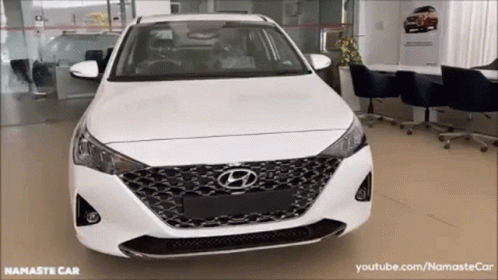 A White Hyundai Car Is Parked In A Showroom With The Words Namaste Car On The Bottom GIF