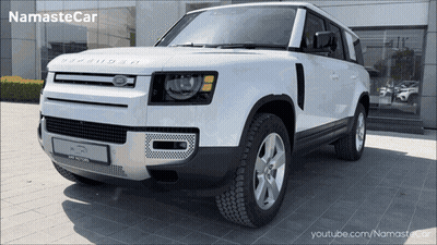 A White Land Rover Defender Is Parked In Front Of A Namaste Car Dealership GIF