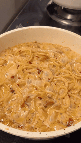 A White Pan Filled With Spaghetti And Sauce On A Stove Top GIF