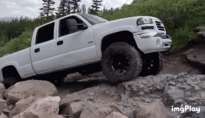 A White Pickup Truck Is Driving Down A Rocky Road . GIF