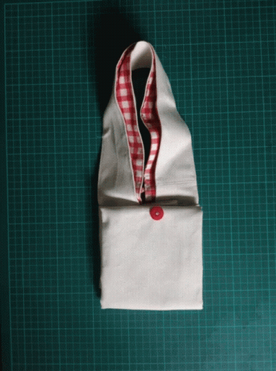 A White Piece Of Fabric With A Red And White Checkered Collar Is Sitting On A Green Cutting Board GIF