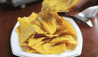 A White Plate Of Nachos With Cheese Being Poured On Top GIF