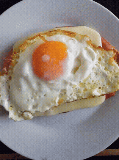 A White Plate Topped With A Fried Egg And A Piece Of Meat GIF