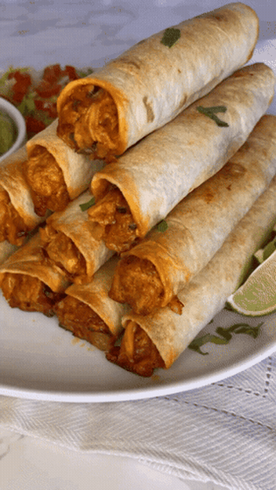 A White Plate Topped With A Stack Of Tacos And Lime Wedges GIF