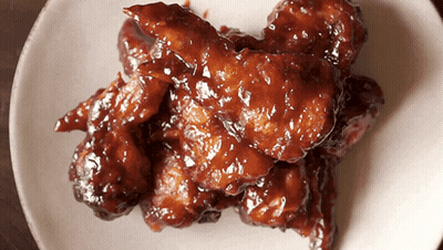 A White Plate Topped With Chicken Wings Covered In A Brown Sauce GIF