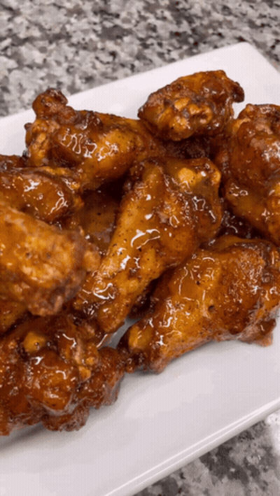 A White Plate Topped With Chicken Wings Covered In A Sauce GIF