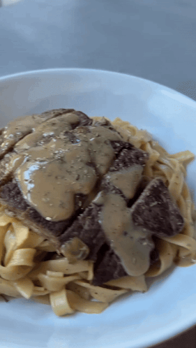 A White Plate Topped With Noodles And Meat With Gravy GIF