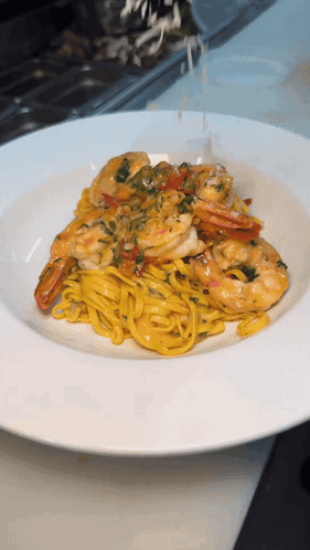 A White Plate Topped With Noodles And Shrimp On A Table GIF