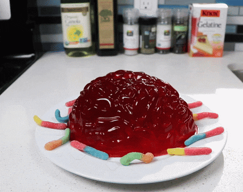 A White Plate Topped With Red Jelly And Gummy Worms With A Box Of Kikin Gelatine In The Background GIF