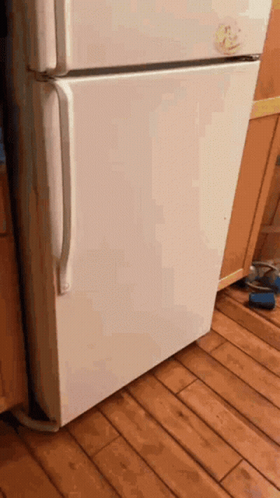 A White Refrigerator Is Sitting On A Wooden Floor Next To A Cabinet GIF