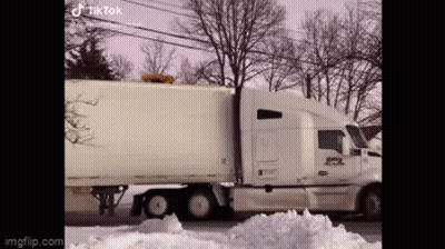 A White Semi Truck Is Driving Down A Snowy Street . GIF