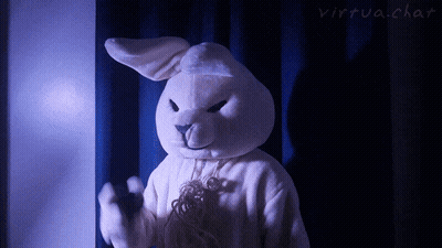 A White Stuffed Bunny Is Standing In Front Of A Blue Curtain GIF